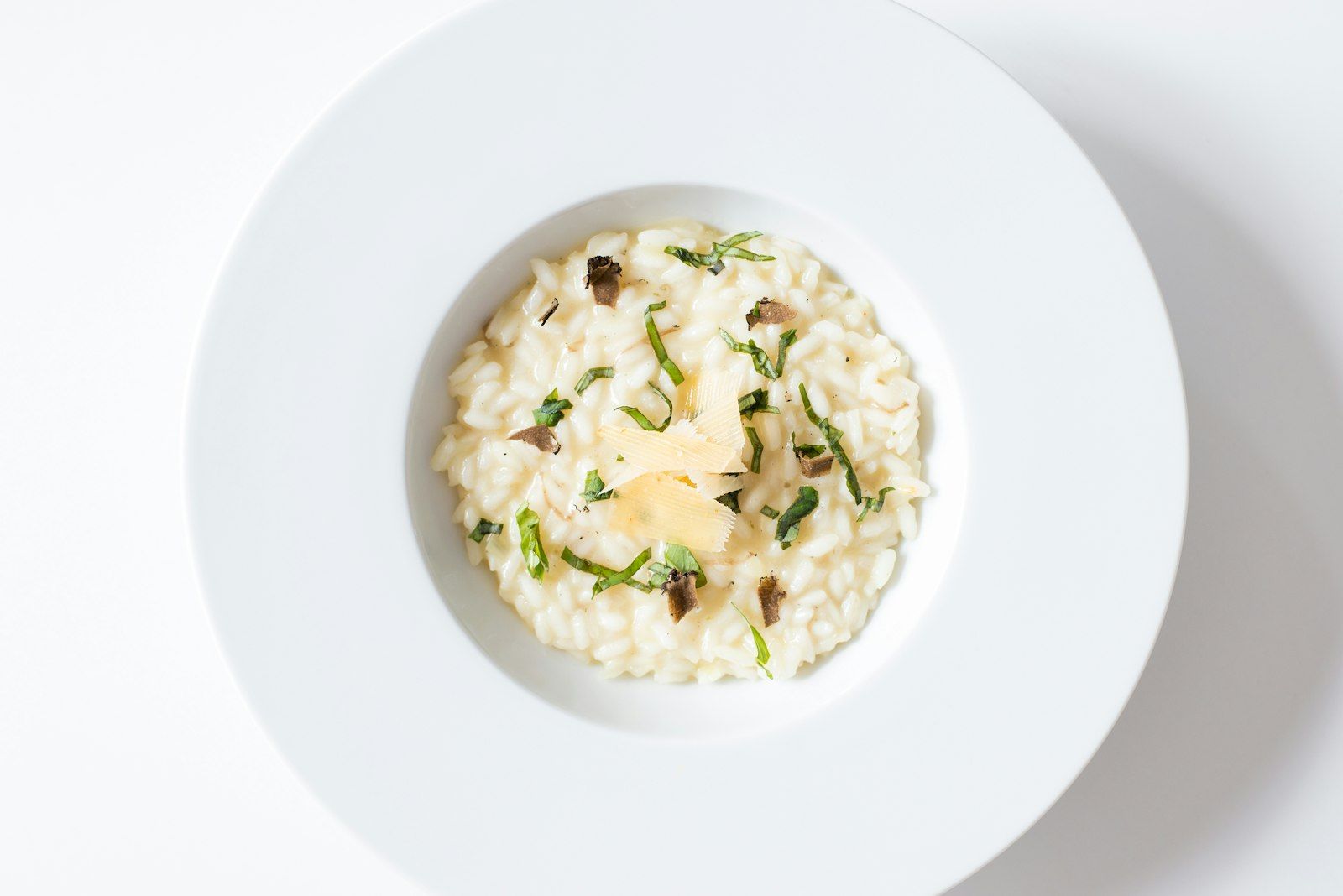 A shallow bowl of creamy pale-green risotto studded with bright peas, finished with shaved parmesan and torn mint leaves.